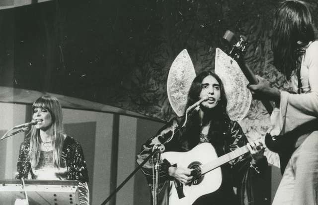  Os Mutantes 2, um grupo musical, composto por dois homens e uma mulher, contando e tocando instrumentos musicais